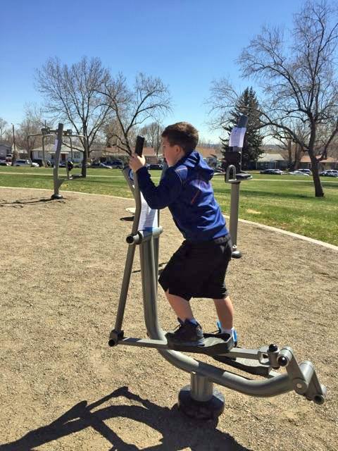 A boy enjoys the outdoor gym equipment, which is located near play structures.