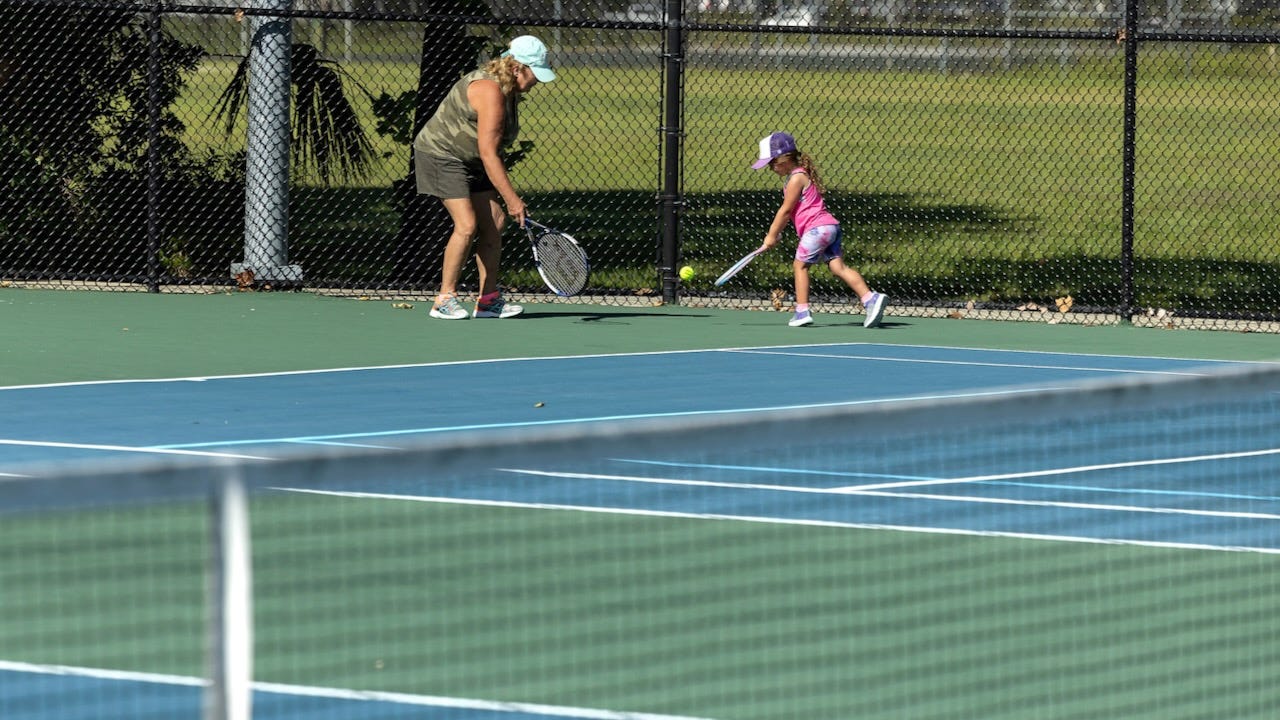 An older woman teaches a young girl how to play tennis