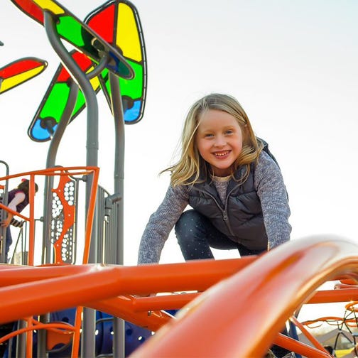 Child climbing on orange climber with shade resembling stained glass in the background