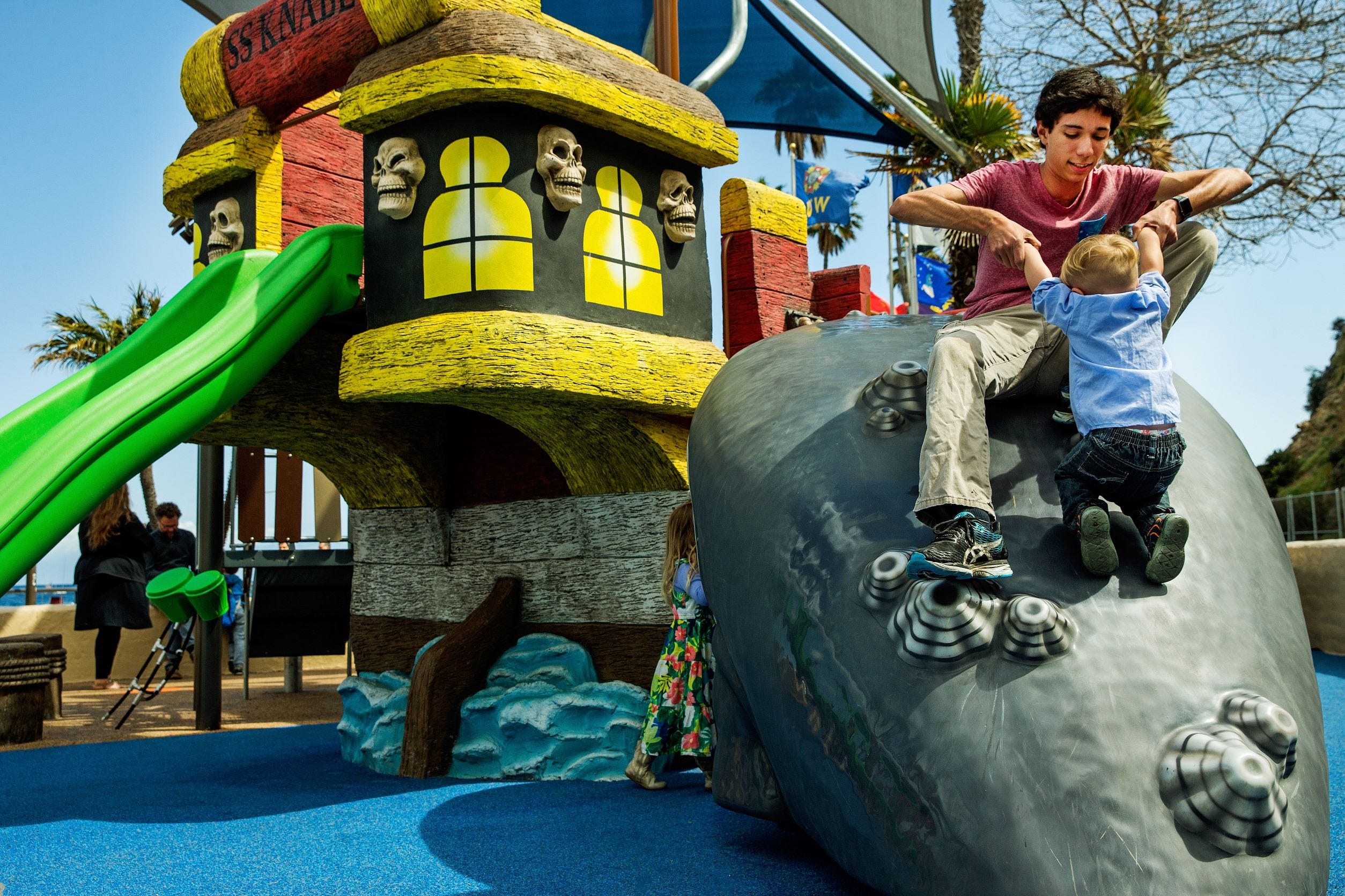 Ocean themed play system with a play ship in the back while a father and son play on a play whale