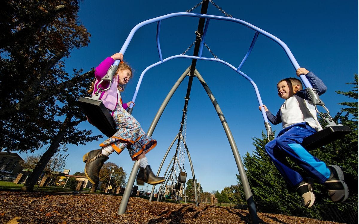 Two children swinging while facing each other in opposing swings